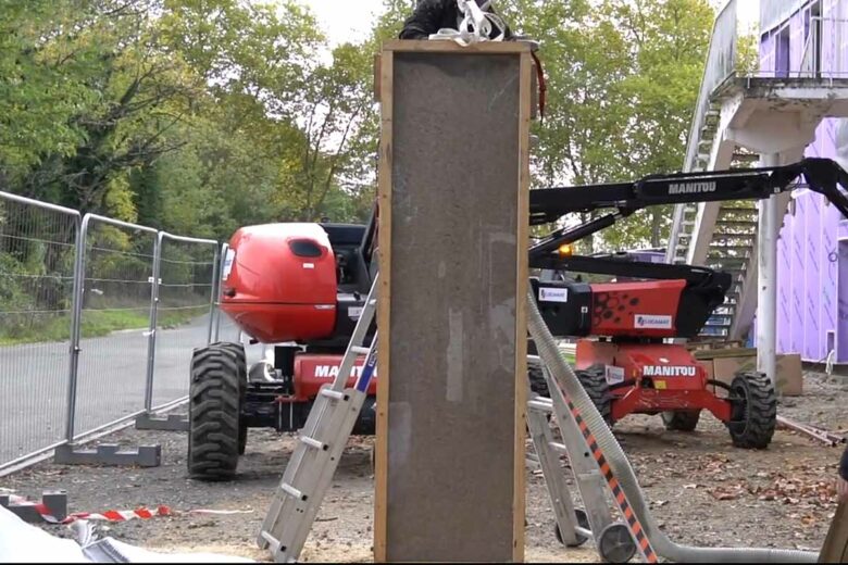 Un panneau isolant est réalisé par insufflation de paille broyée lors d'un chantier.