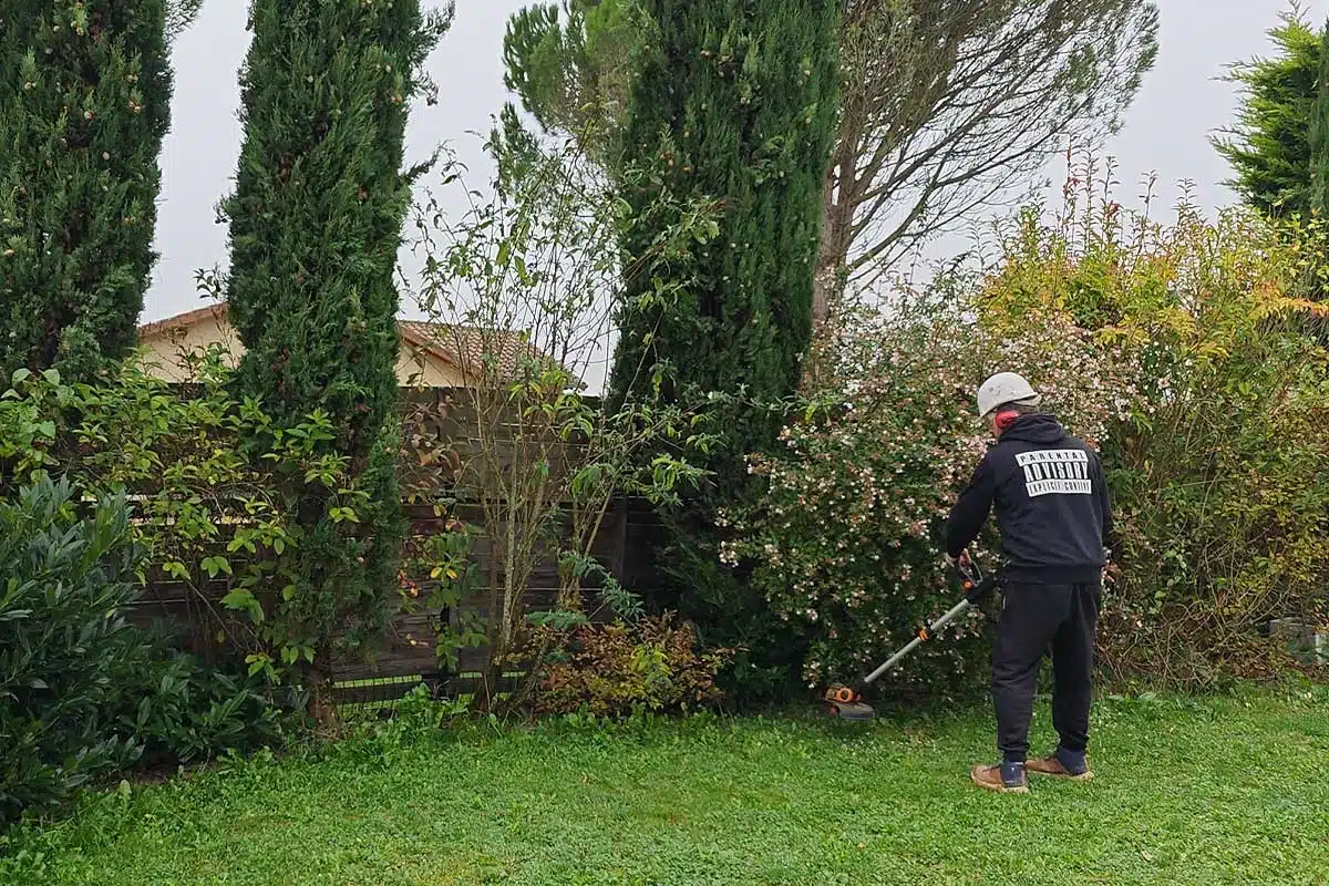 Un homme passe la débroussailleuse.