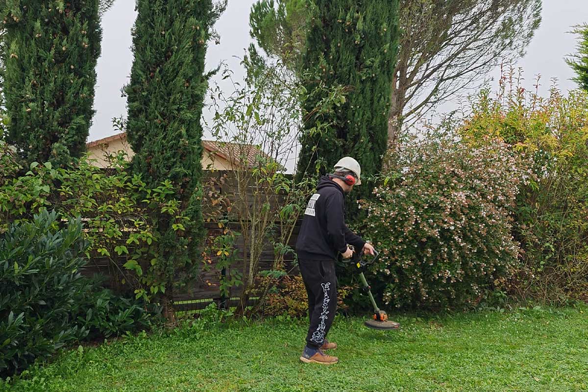 Un homme débroussaille un jardin.