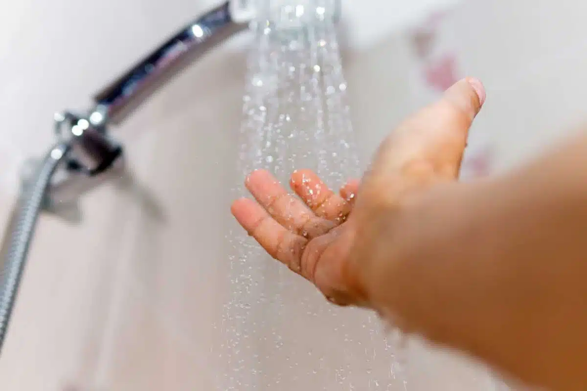 Une main vérifie la température de l'au de la douche.