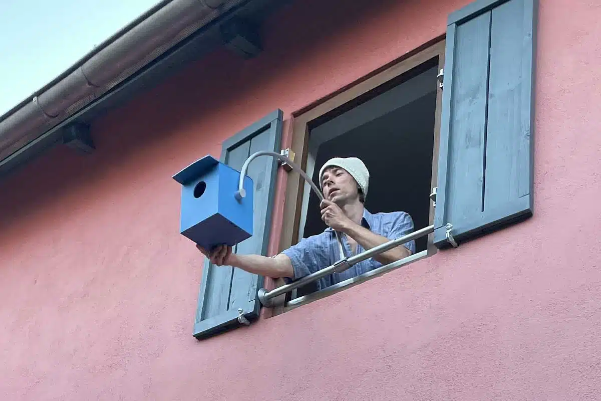 Un homme fixe un nichoir à une fenêtre.