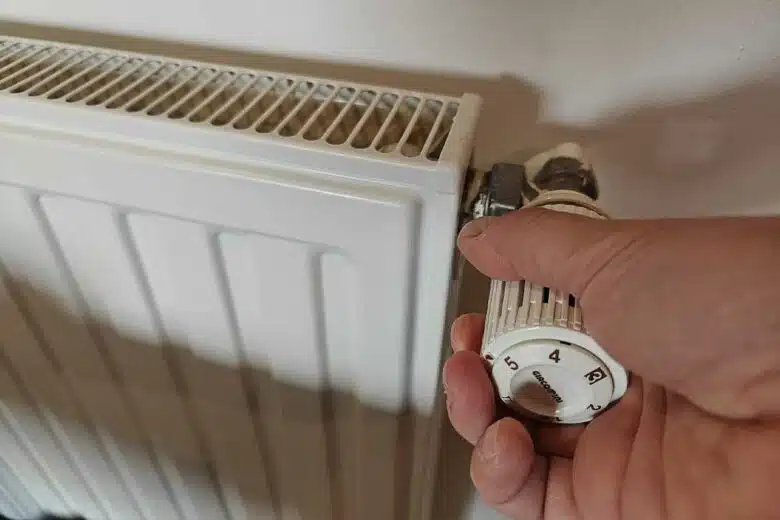 Un homme règle le thermostat d'un radiateur.