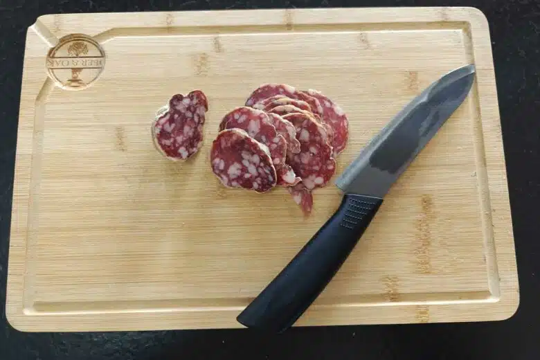 Une planche à découper en bois avec quelques tranches de saucisson.