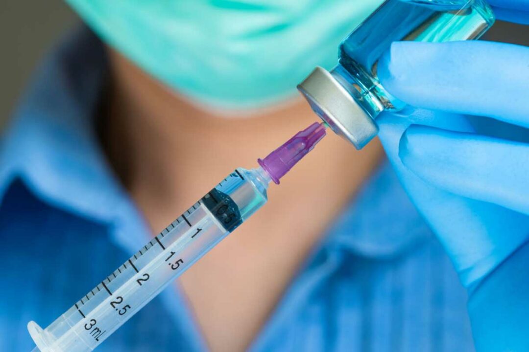 Une infirmière qui tire une dose de vaccin dans un flacon avec une seringue.