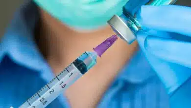 Une infirmière qui tire une dose de vaccin dans un flacon avec une seringue.