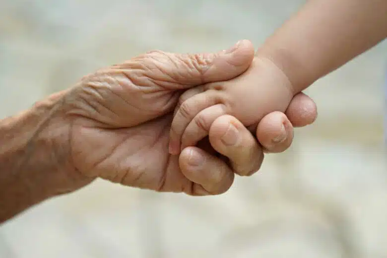 La main d'une personne âgée tient la main d'un enfant.