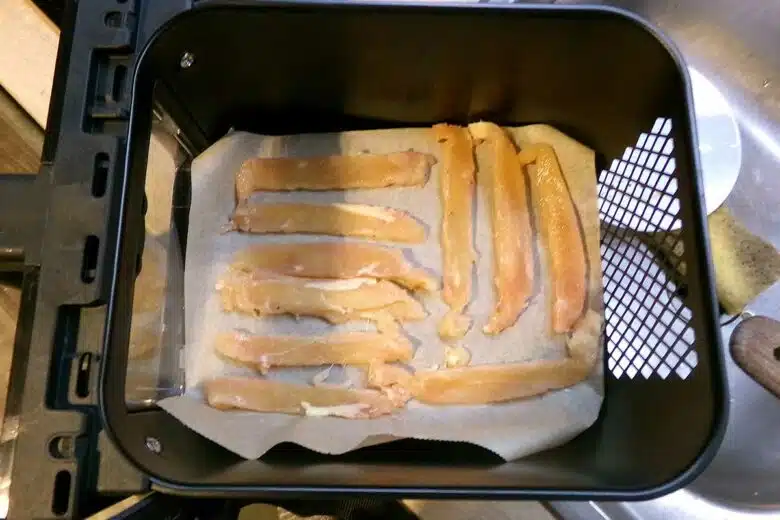 Des lamelles de blanc de poulet dans un panier d'airfryer.