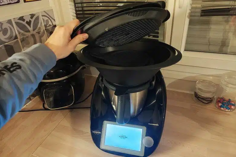 Un Thermomix dans une cuisine, une main soulève le couvercle.