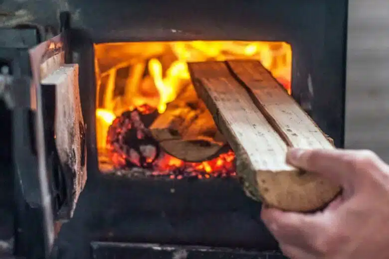 Une personne insert une buche dans son poêle.