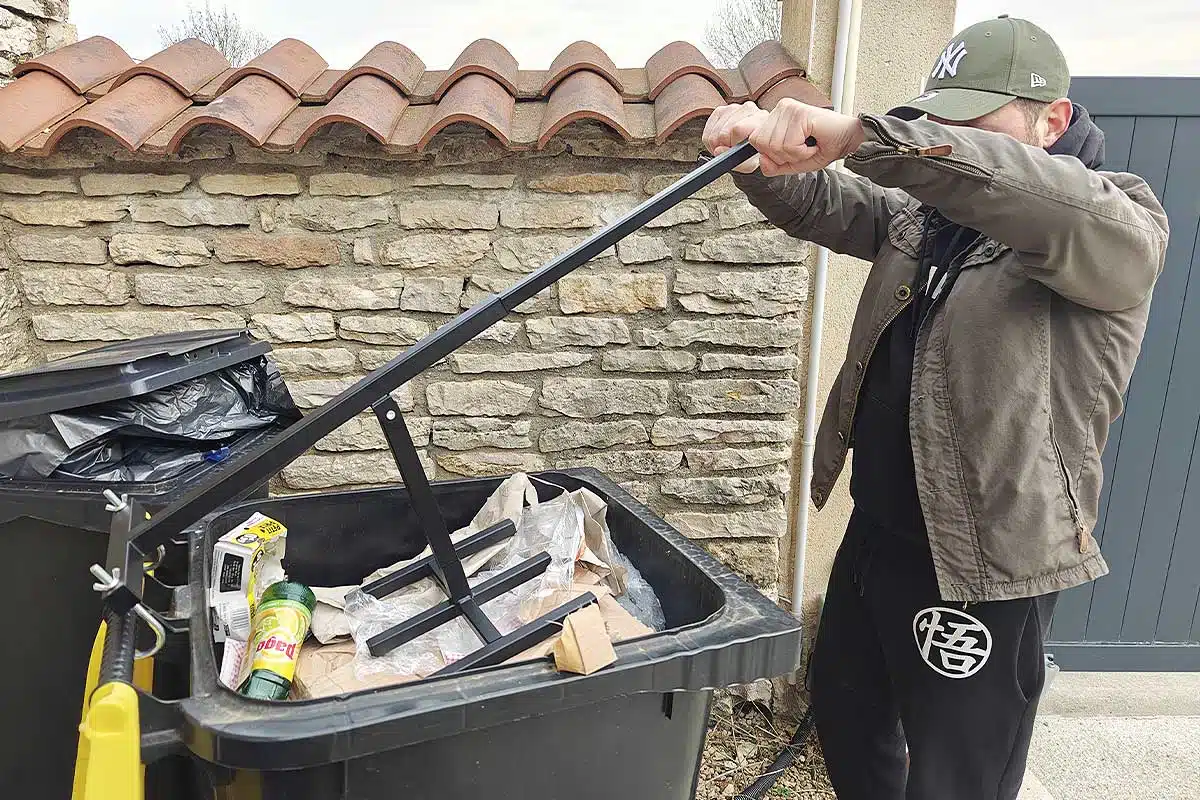 Un homme compacte ses poubelles pour réduire leur volume.