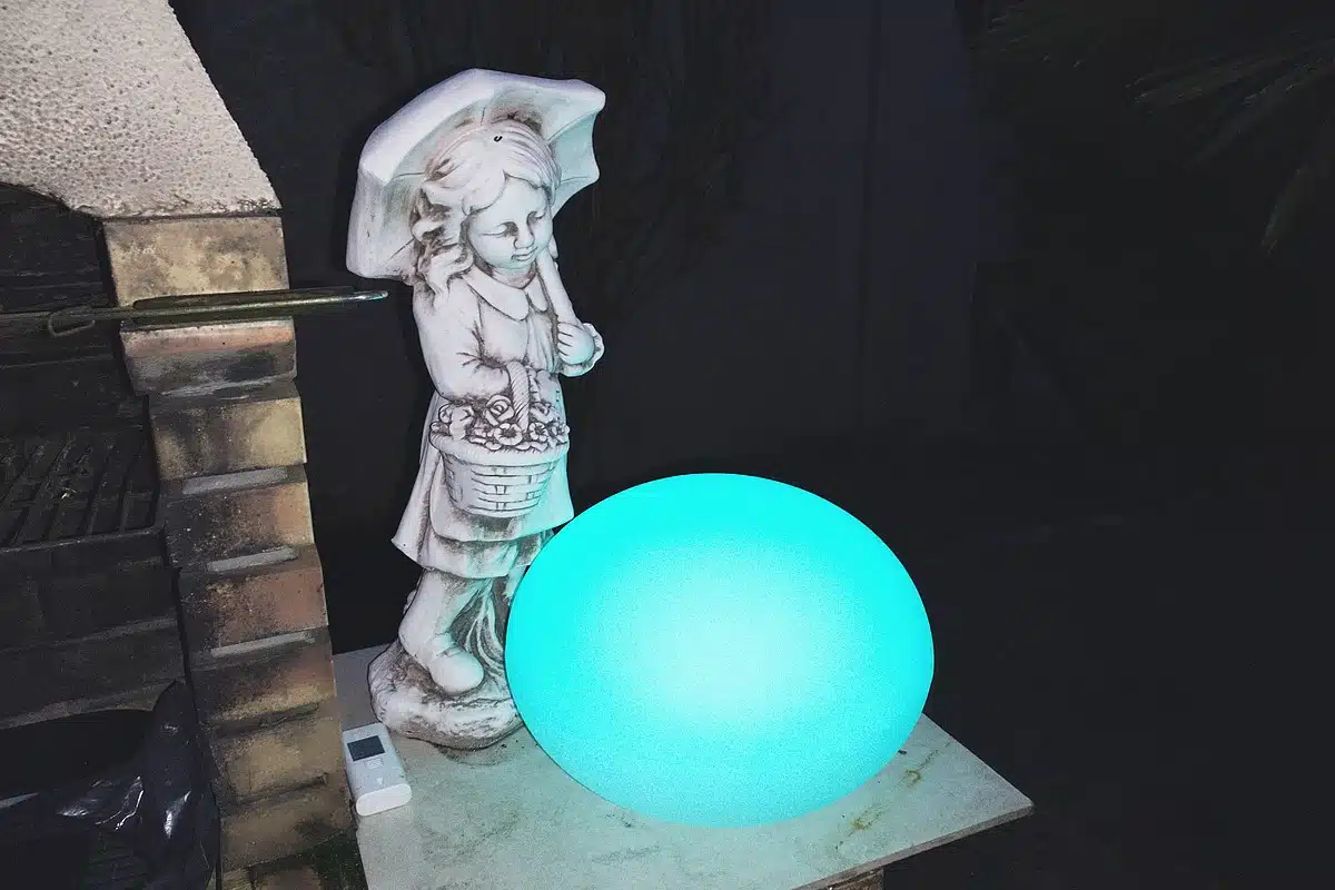 Le Galet GuirLED illumine l’extérieur avec une belle lumière bleue, posé près d’une statue sous un parapluie.