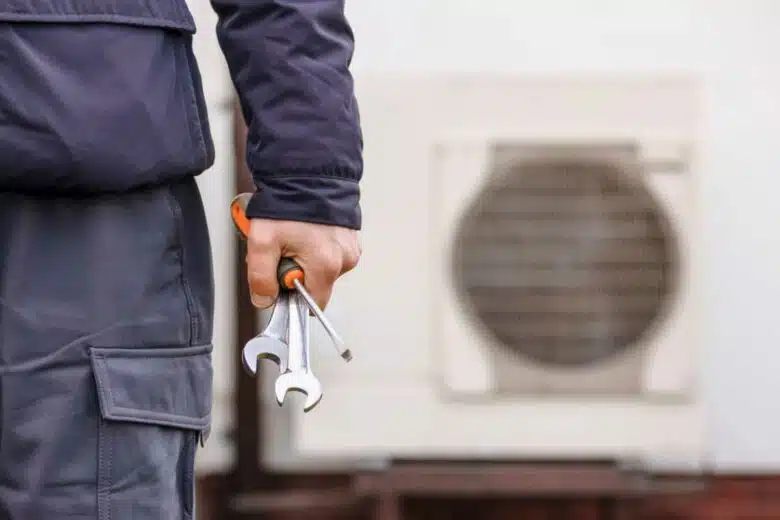 Un homme tient des outils devant une pompe à chaleur.