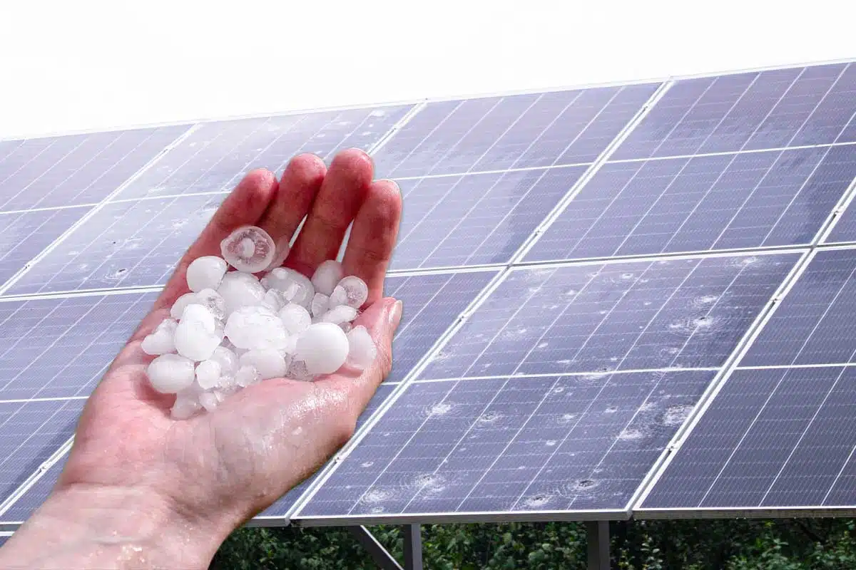 Une main tenant des grêlons et des panneaux solaires cassés.