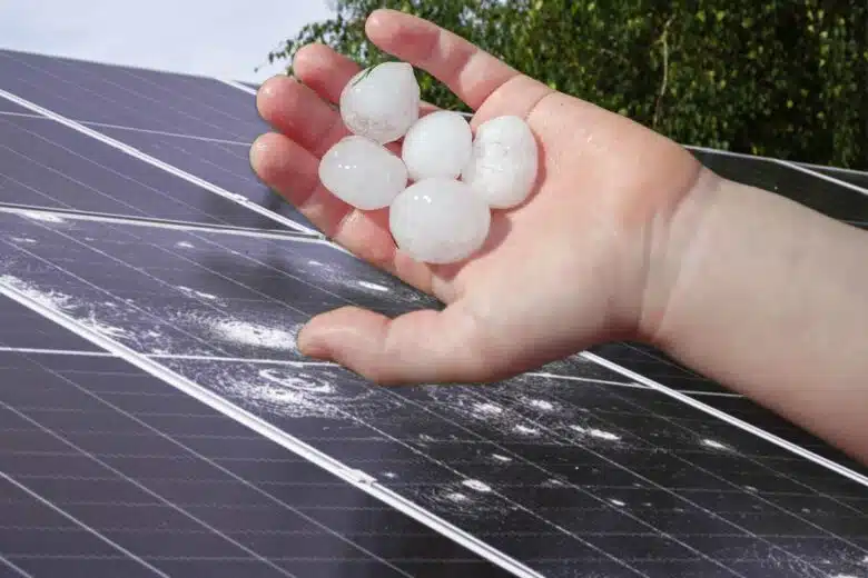 Une main tenant des grêlons et des panneaux solaires cassés.