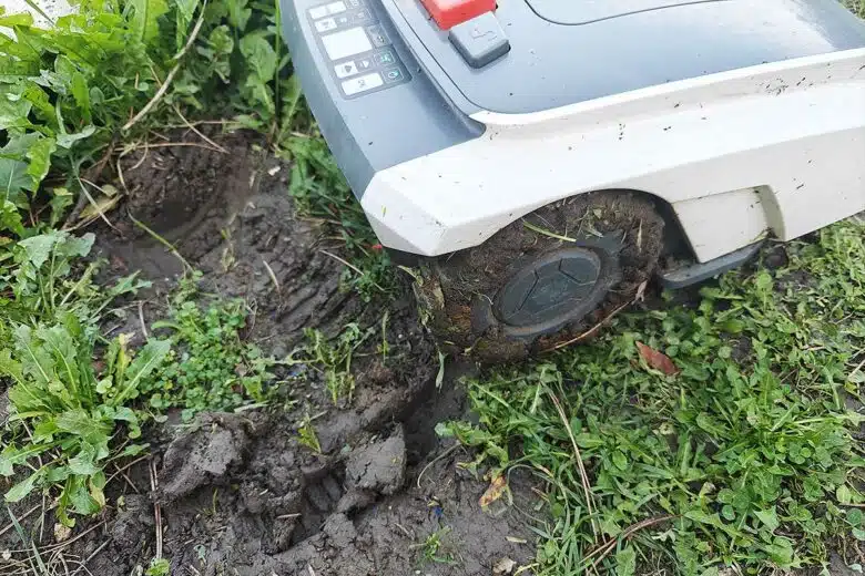 Un robot tondeuse sur un terrain boueux.